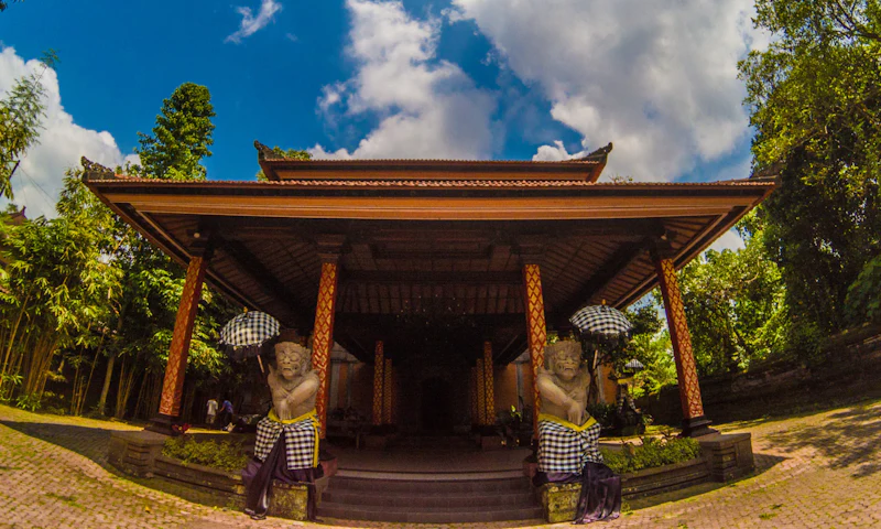 A traditional building with decorative columns, flanked by statues holding umbrellas, under a blue sky with clouds.