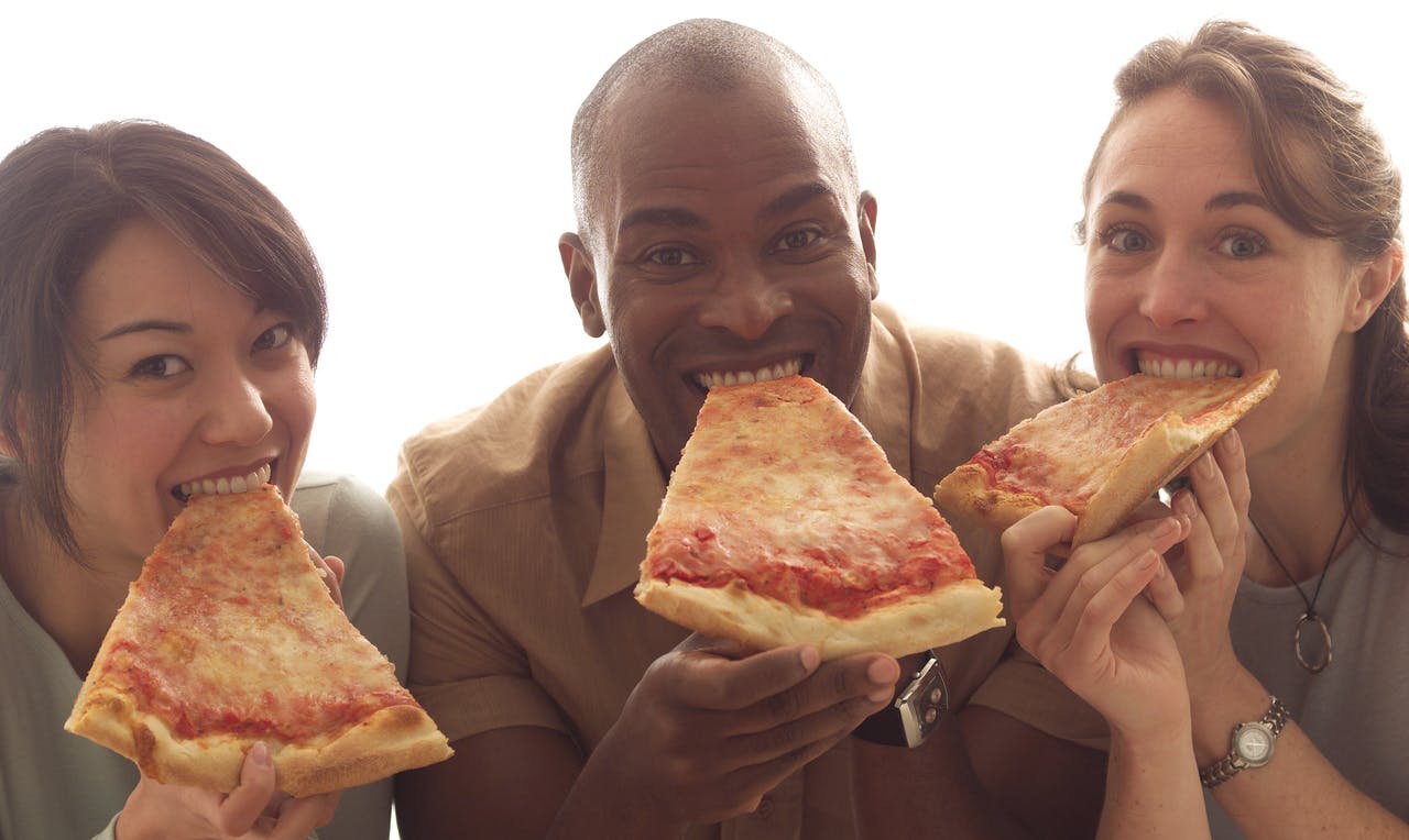 A smiling man and woman, each holding and about to eat a large slice of cheese pizza.