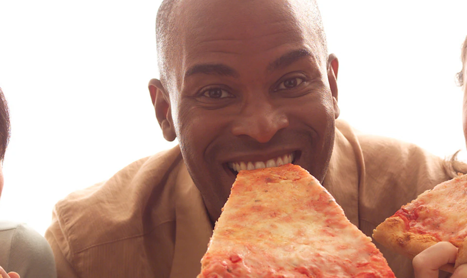 A smiling man and woman, each holding and about to eat a large slice of cheese pizza.