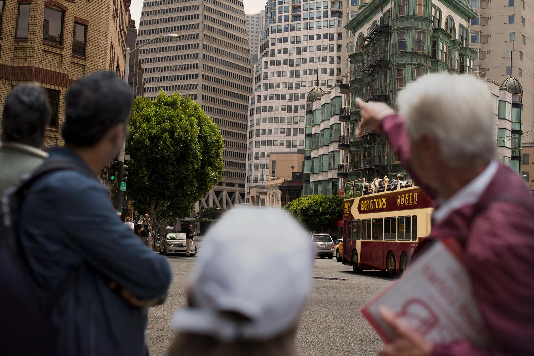 前景には大勢の人々が集まり、背の高い建物、交通、木が背景にある都会のストリートシーン。