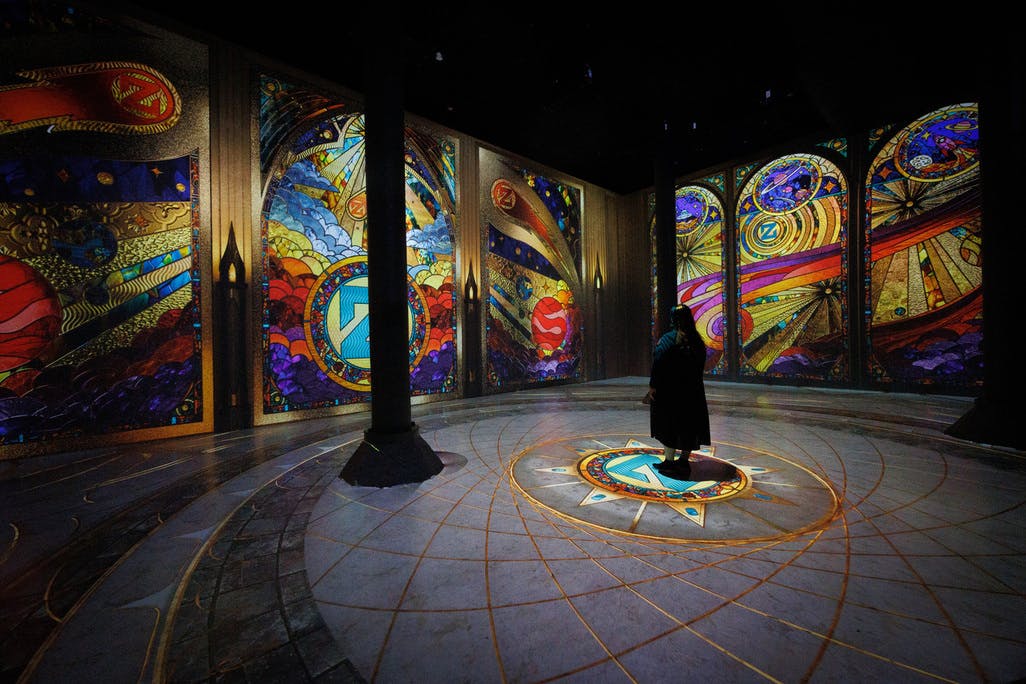 Eine Person steht in einem Musikstudio voller Instrumente, darunter Gitarren, ein Klavier, ein Schlagzeug und Verstärker.