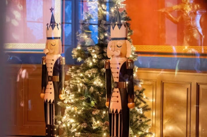 To nøddeknækkerstatuer står på hver side af et tændt juletræ i et festligt indrettet rum.