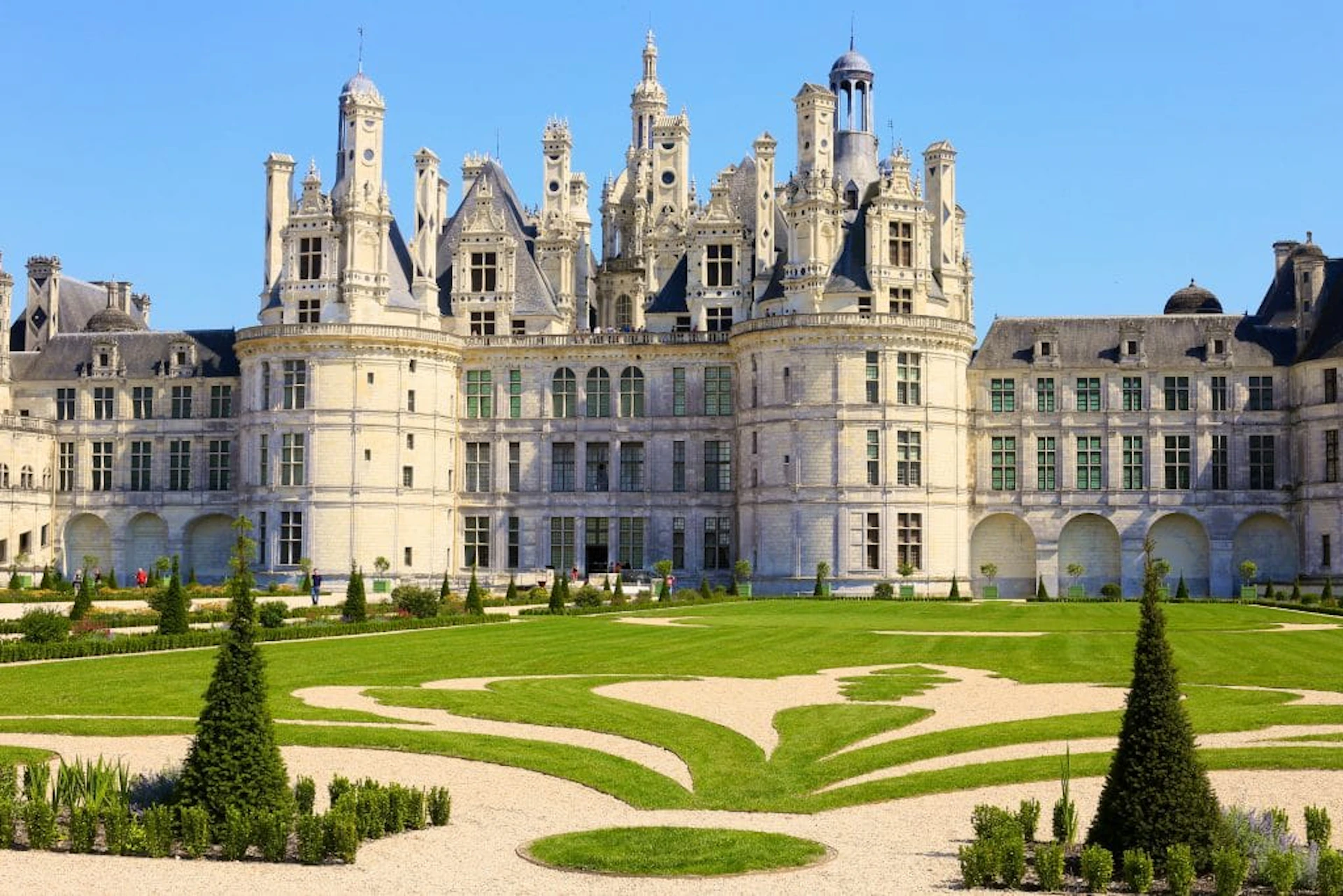 A grand castle with ornate towers and a manicured garden featuring geometrically designed grass and pathways.