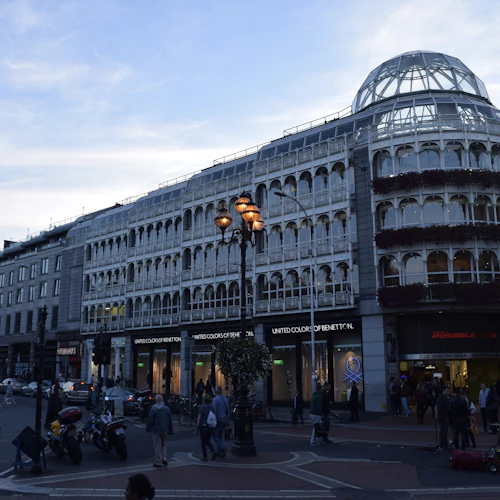 Gatuvy av en flervåningsbyggnad med välvda fönster, skyltfönster av United Colors of Benetton och människor som går.
