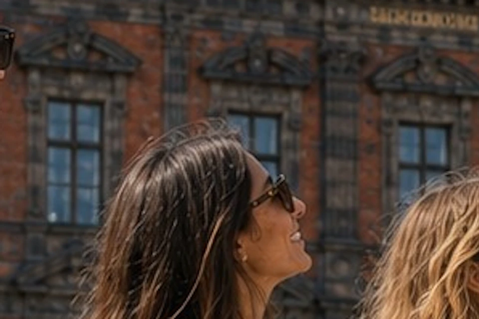 Three people standing in a plaza with a historic brick building in the background, one pointing towards the sky.