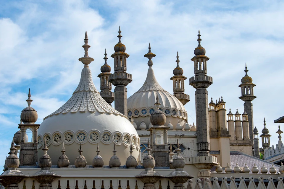 Ornate domes and minarets of a white palace with detailed carvings and a blue sky in the background.