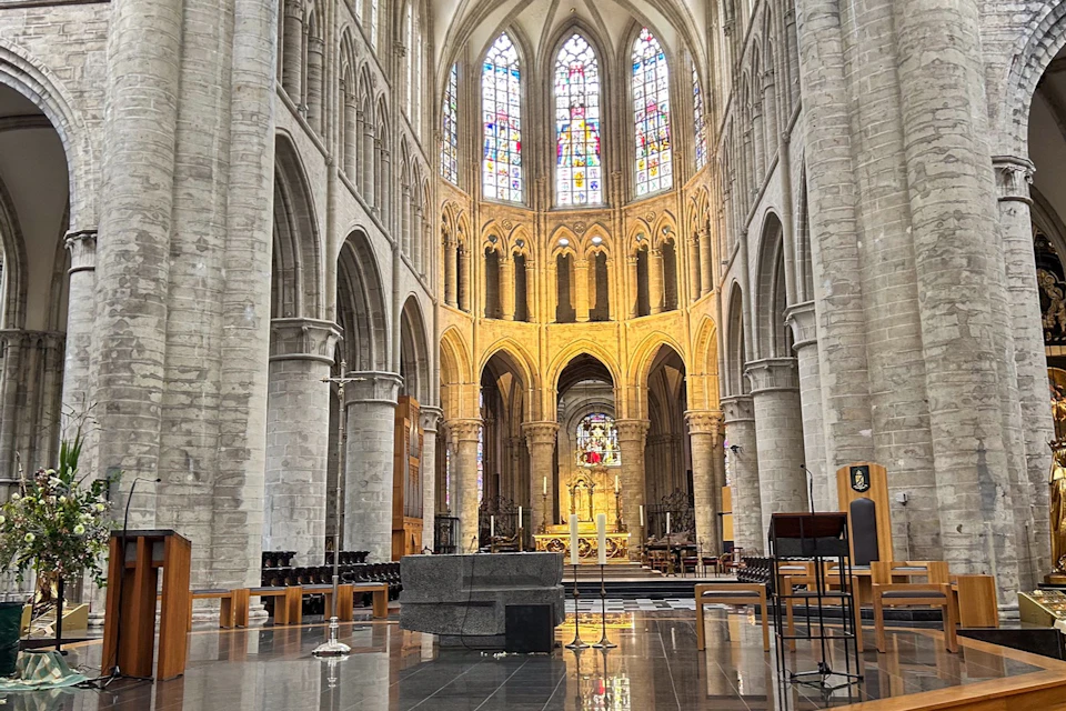 Interior of a grand cathedral with high vaulted ceilings, stained glass windows, and a central altar with ornate details.