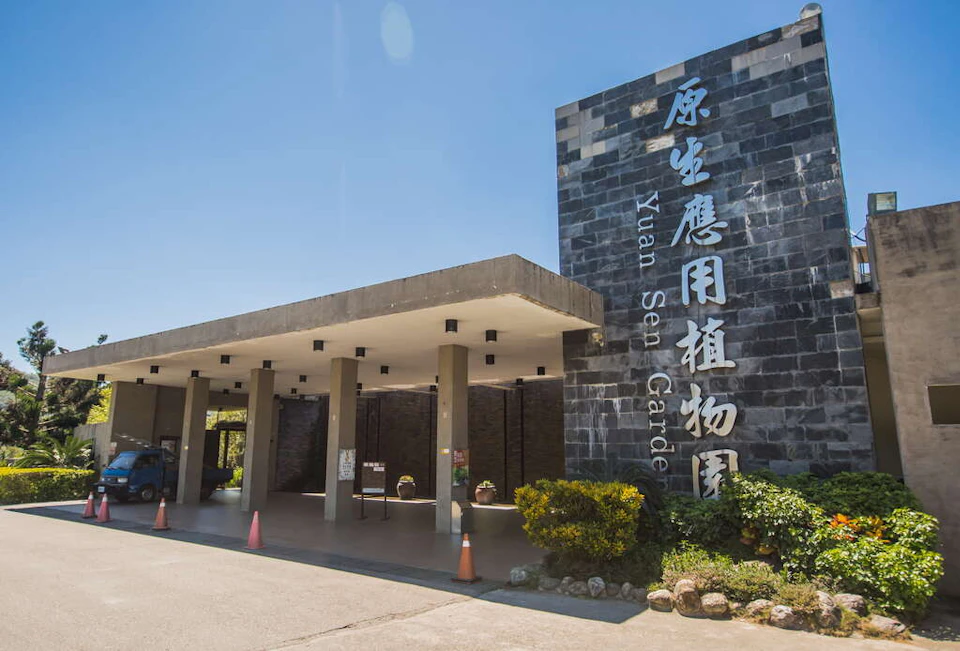 Entrance of Yuan Sen Garden with a modern building, signage, and plants under a clear blue sky.