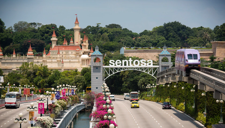 A road leading to Sentosa with a decorative arch, flowers, and a castle-like building in the background.