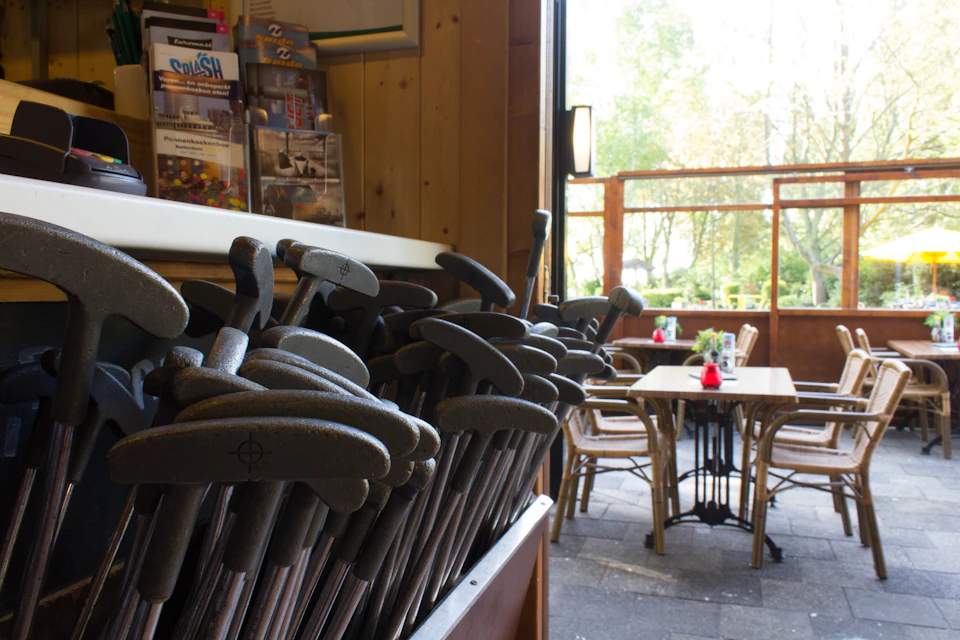 A pile of putters in a rack inside a wooden structure, with an outdoor seating area and tables visible through an open window.