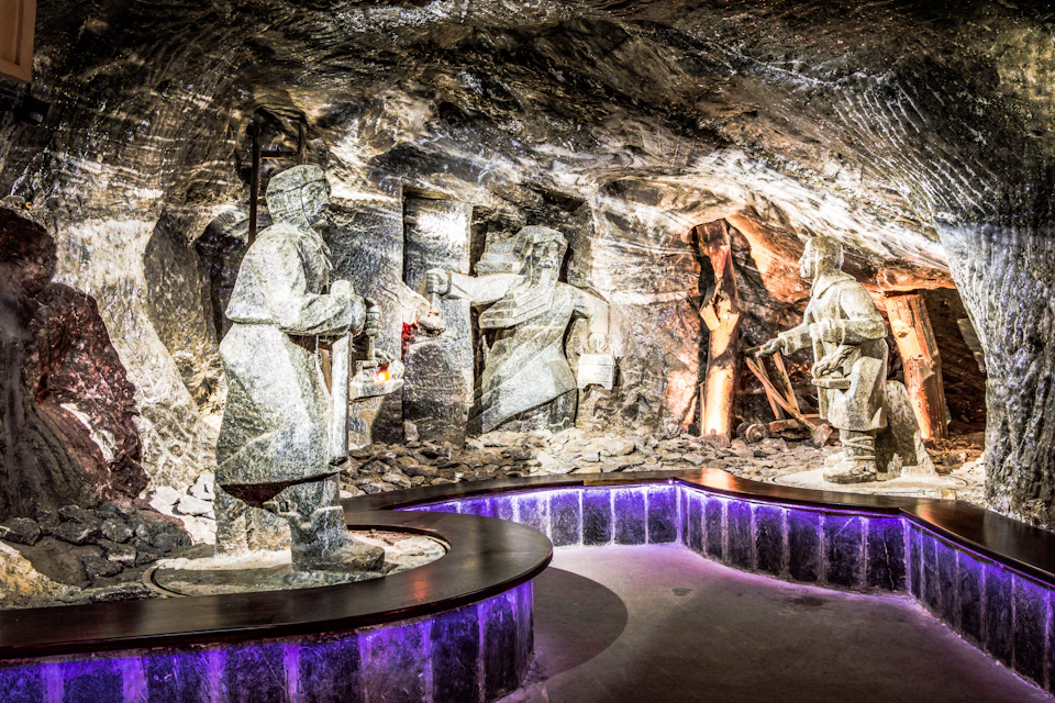 Stone sculptures of miners working in a dimly lit cave, with illuminated purple light accents on a curved display platform.