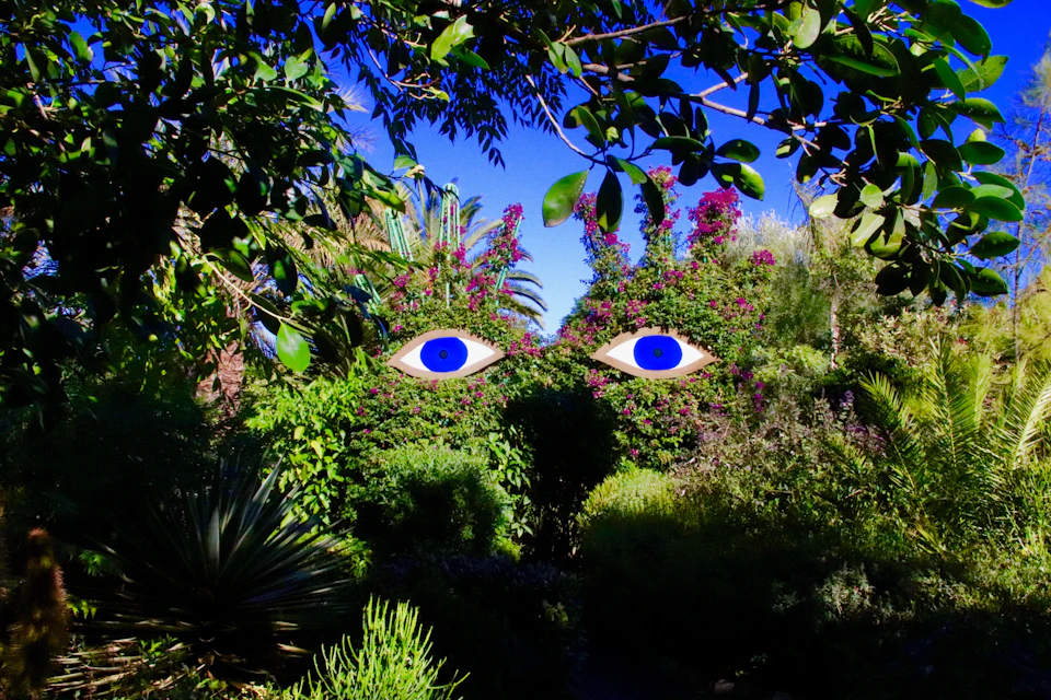 A lush garden scene with vibrant greenery and flowers, featuring two stylized blue eyes digitally superimposed in the sky.