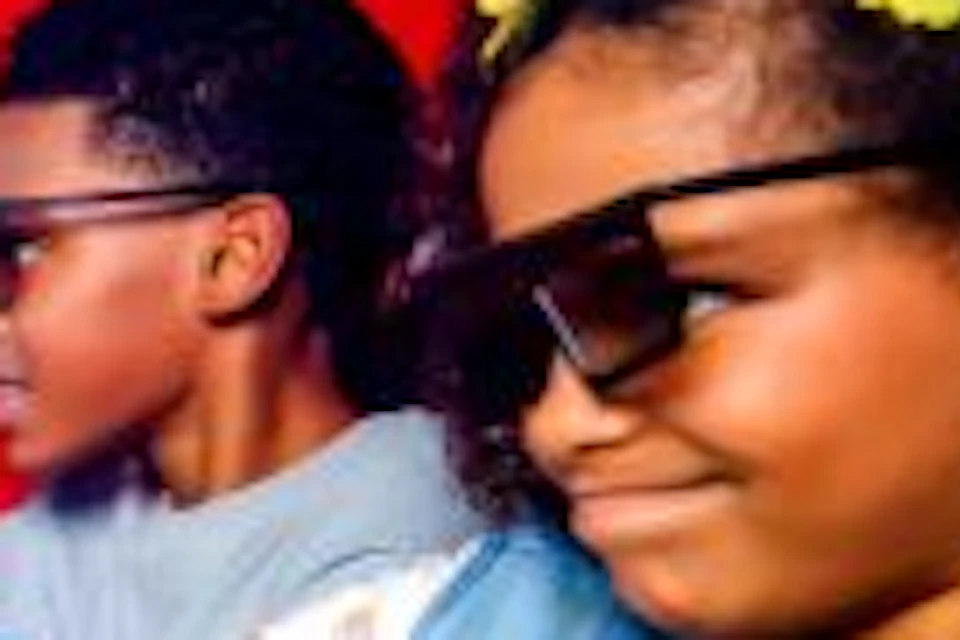 Two children wearing 3D glasses interact with a brightly lit, colorful arcade game in a dark room.