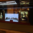 Display case with framed paintings, including the Mona Lisa and The Last Supper, under soft lighting.