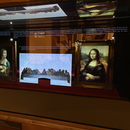 Display case with framed paintings, including the Mona Lisa and The Last Supper, under soft lighting.