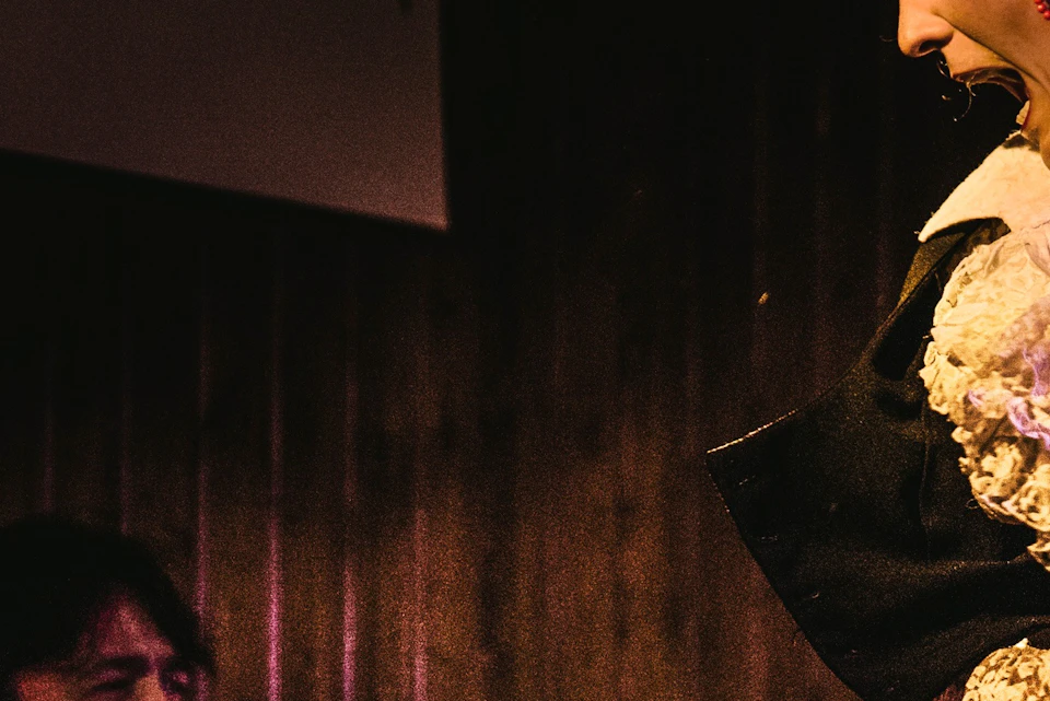 A performer singing or shouting passionately, wearing traditional Spanish-style clothing, under dramatic lighting on stage.