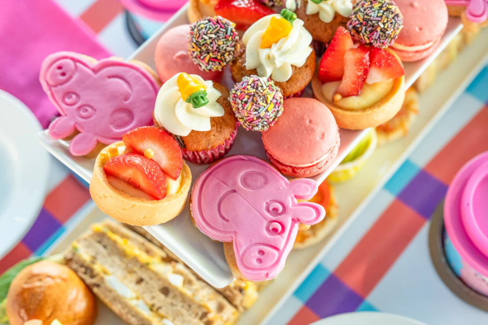 A colorful assortment of desserts, including cupcakes with icing, macarons, and pink animal-shaped cookies on a platter.