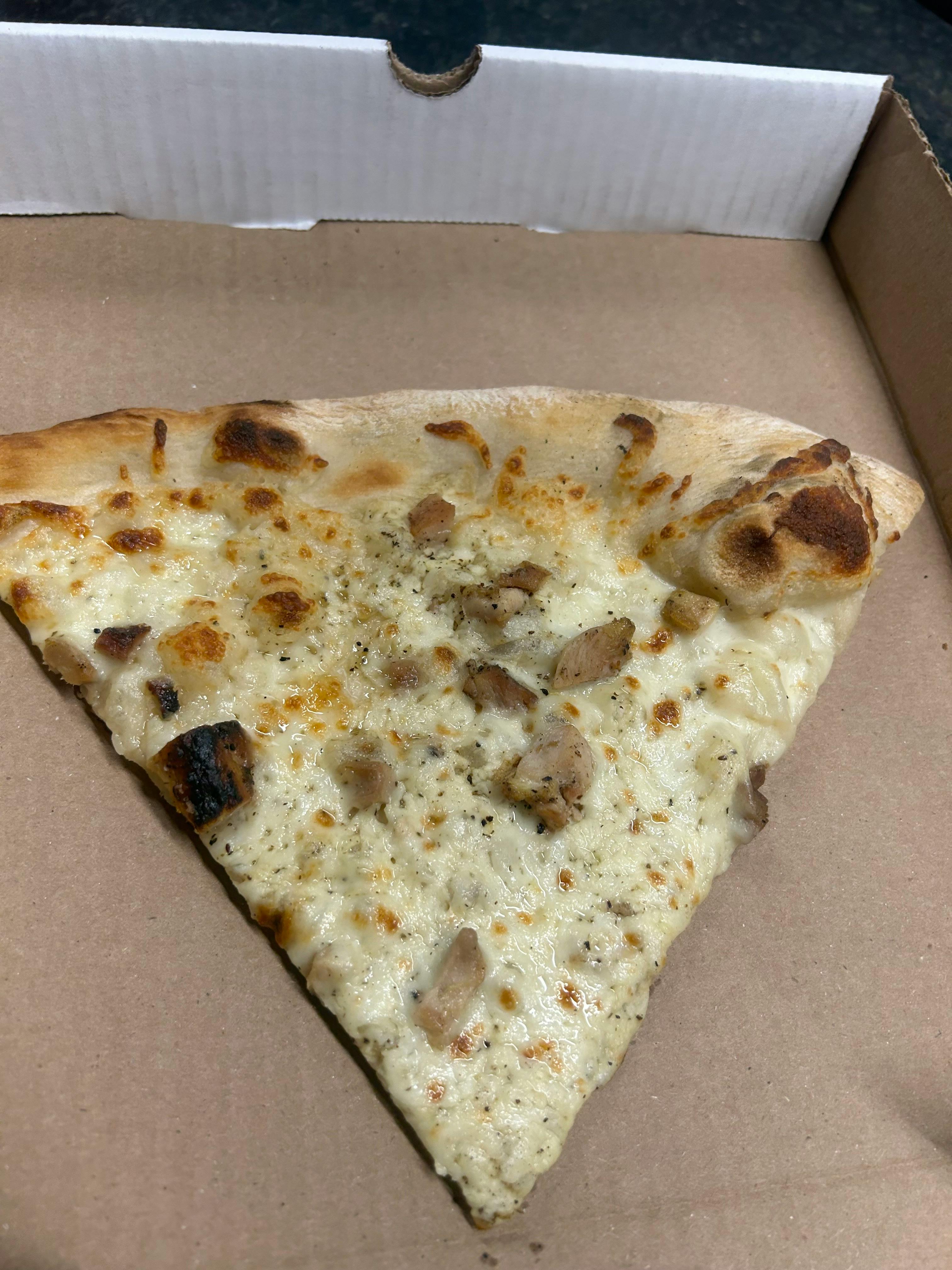 갈색 판지 포장에 구운 치킨 조각이 담긴 흰색 피자 한 조각.