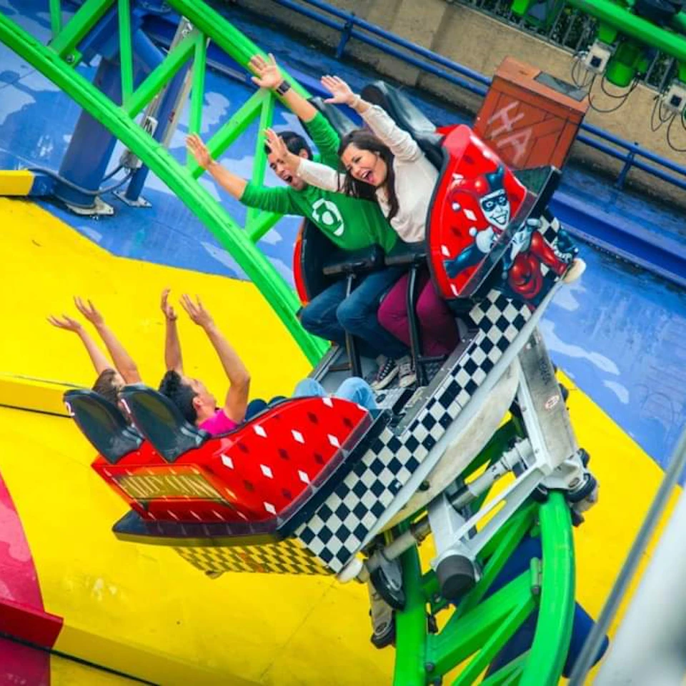 People riding a colorful rollercoaster with raised arms, featuring a checkerboard and comic-style design elements on the ride.