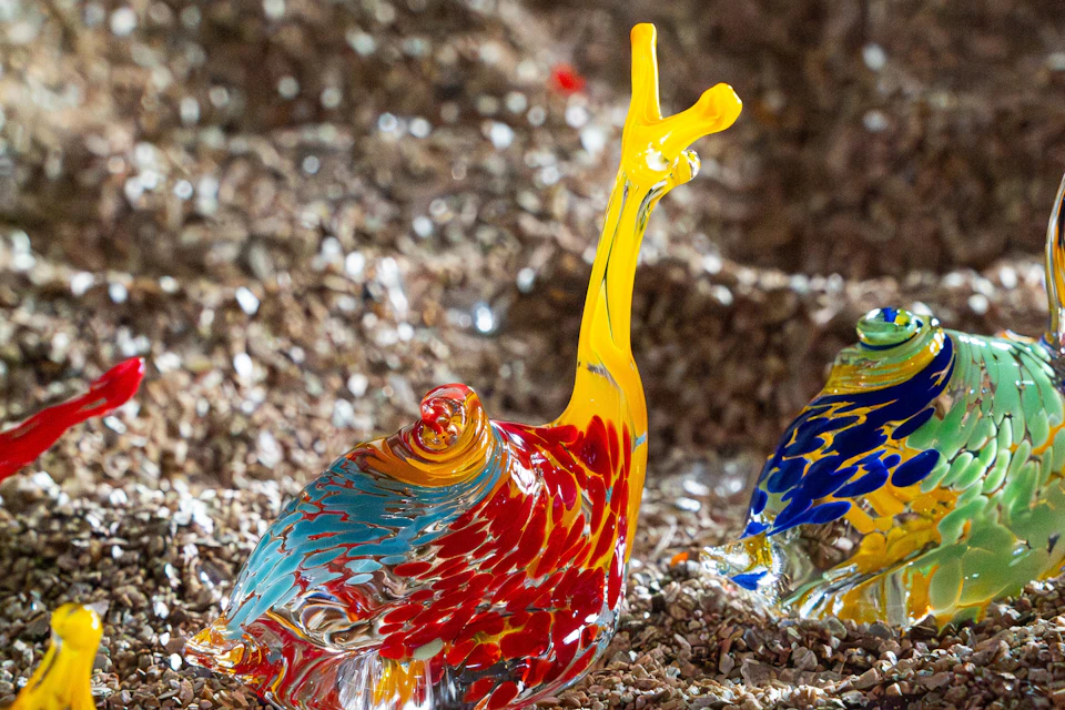 Colorful glass sculpture of a snail with a yellow antennae and red, blue, and orange body on a textured surface.