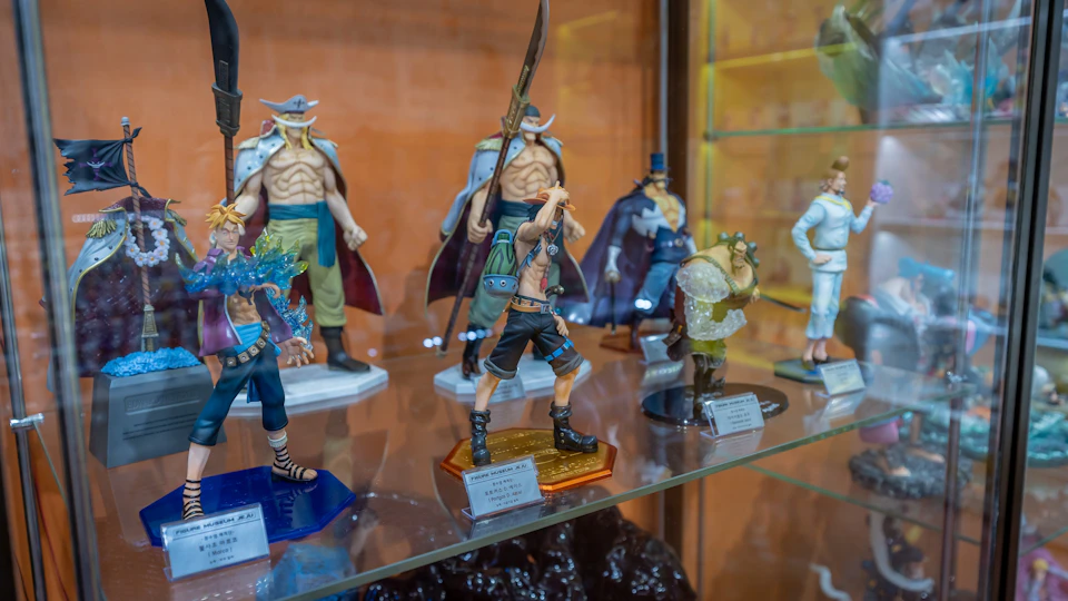A display of anime character figurines on a glass shelf, featuring detailed designs and vibrant colors.