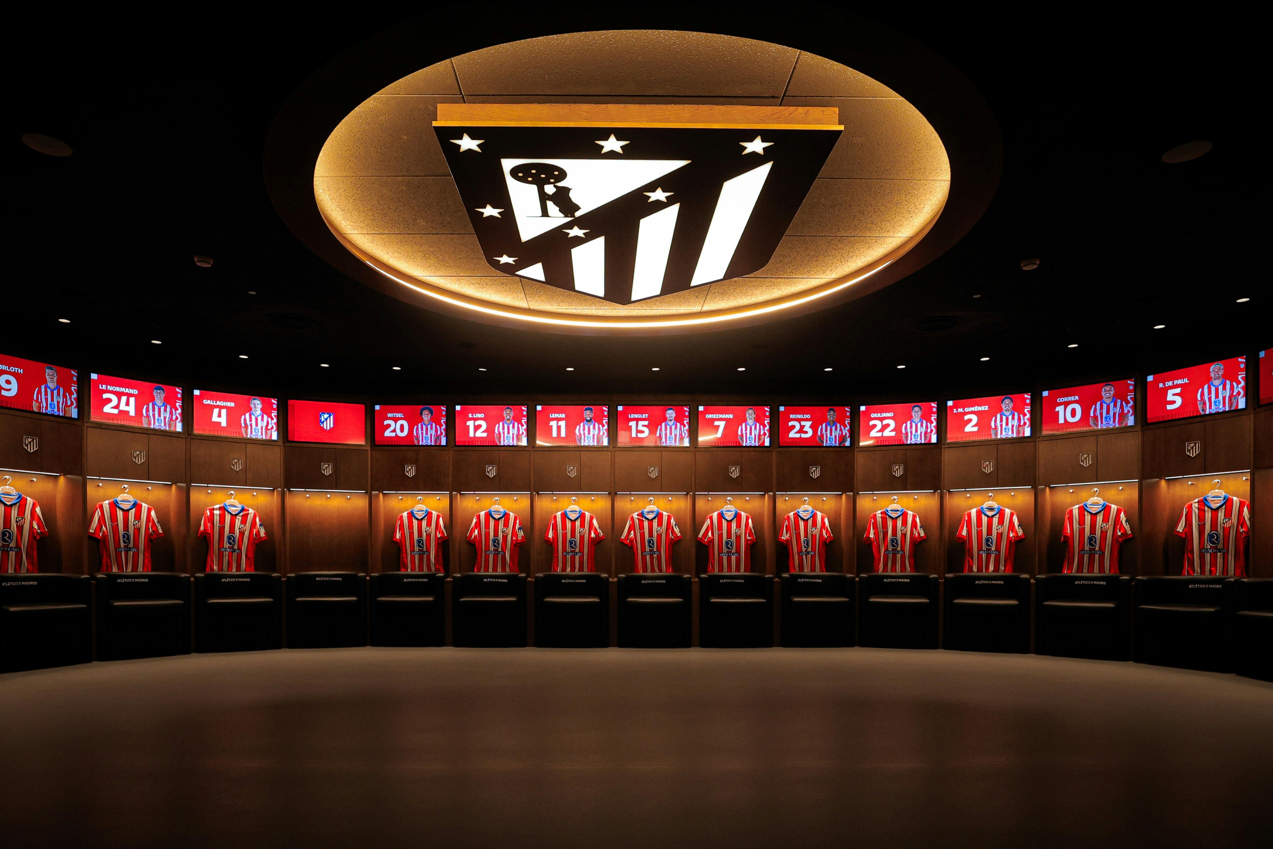 Uno spogliatoio con maglie a strisce bianche e rosse disposte sotto cubicoli illuminati e un logo sul soffitto.