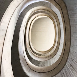 En spiralformad betongtrappa i flera nivåer sedd underifrån, som visar upp dess organiska, böjda design och lager.