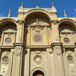 Facade of a historic cathedral with ornate stone carvings, arched windows, and a large central circular design under a blue sky.