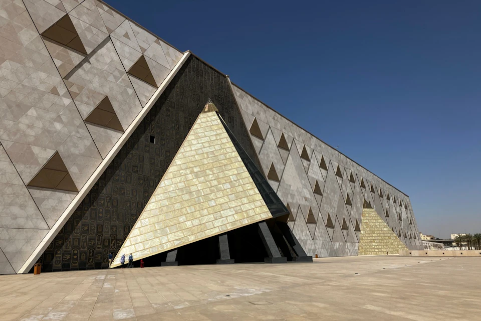 A modern building featuring triangular patterns and a large entrance shaped like a pyramid, with a clear blue sky above.