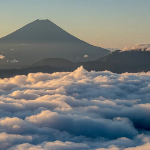 A mountain peak rises above a sea of clouds at sunrise, with a clear sky in the background.