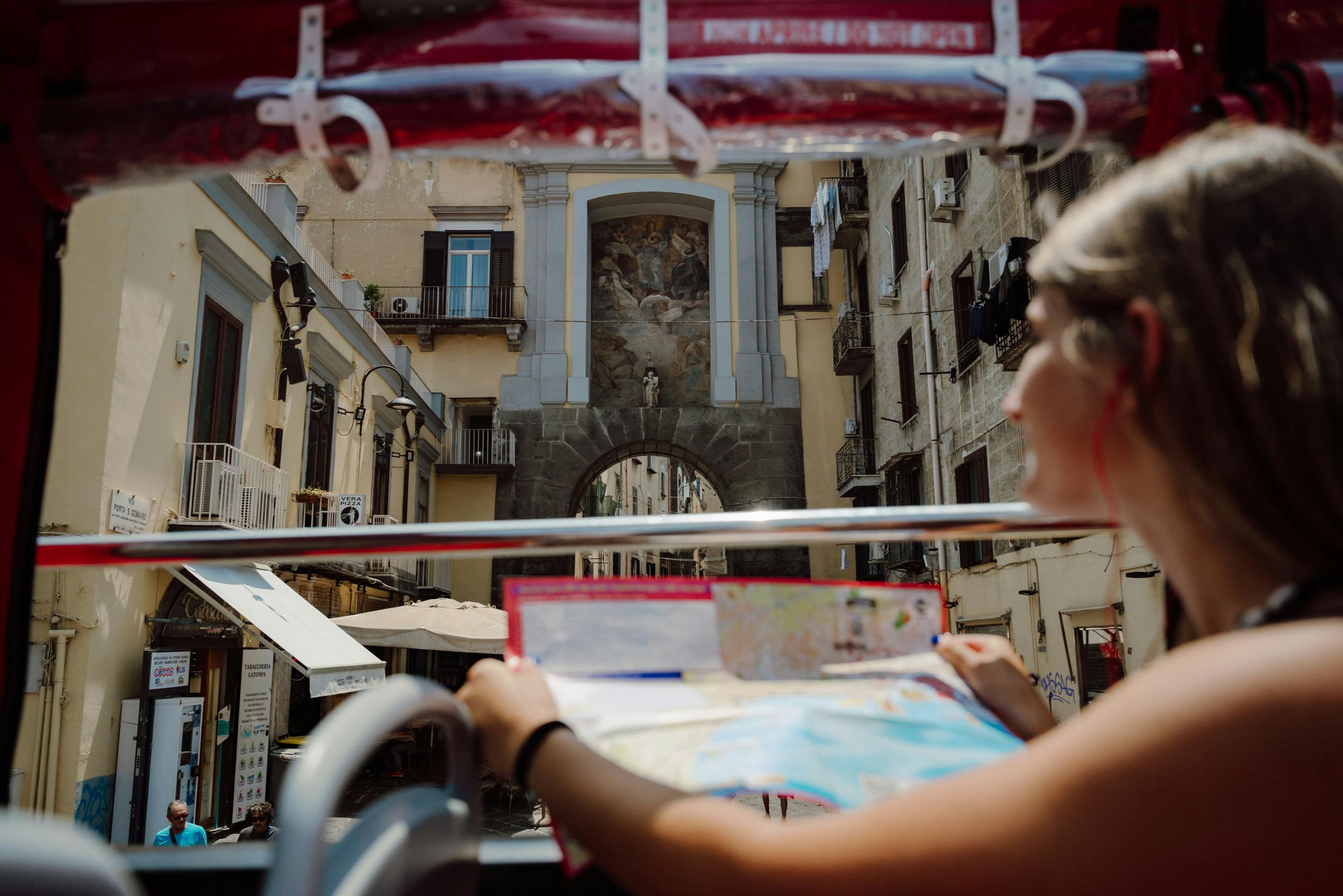 Una persona che tiene in mano una mappa su un autobus scoperto, con una vista di un arco ornato e di edifici sullo sfondo.