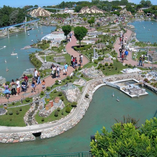 Veduta aerea di un parco in miniatura con edifici modello, sentieri, giochi d'acqua e visitatori che camminano e osservano le miniature.