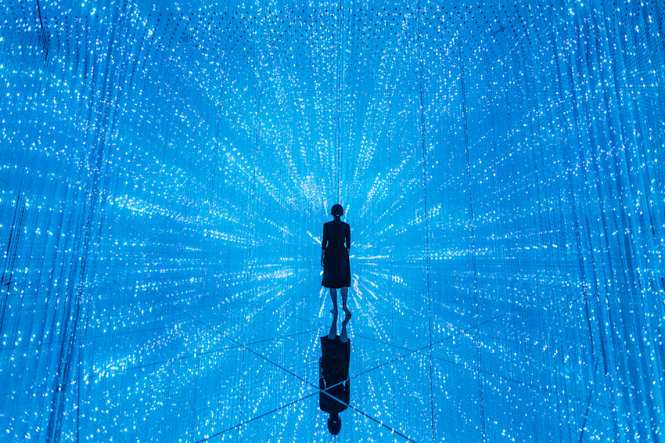 A person stands in a room surrounded by blue LED lights, creating a starburst pattern with reflections on the floor.