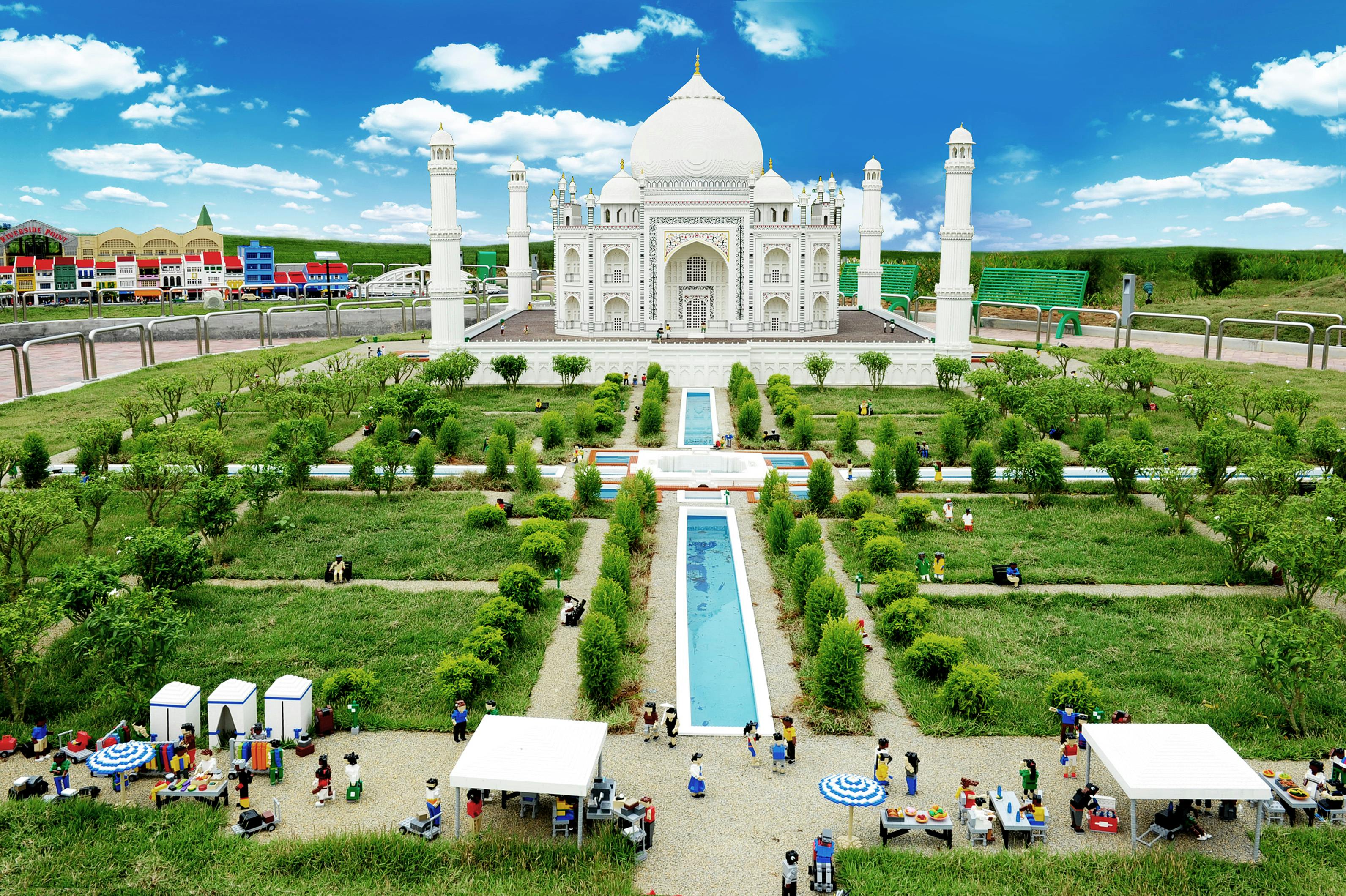 Miniature Taj Mahal replica with gardens and reflective pools. Figures of people are scattered throughout the park, creating a lively scene.