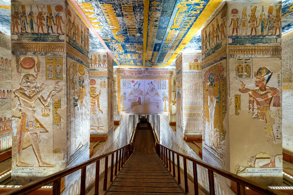 A richly decorated corridor of an ancient Egyptian tomb with painted walls and ceiling, featuring hieroglyphs and figures.