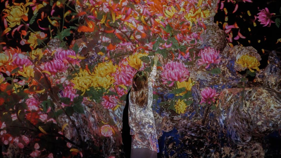 Una persona amb un vestit de colors clars s'acosta a una projecció de flors i vegetació a la paret de colors vius i acolorits.