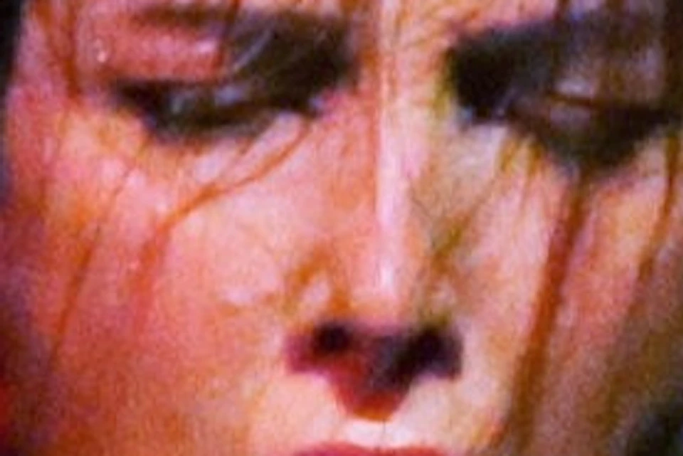 A woman performing intensely in front of a stone wall, wearing a black shawl, red and white attire, and a red hairpiece.