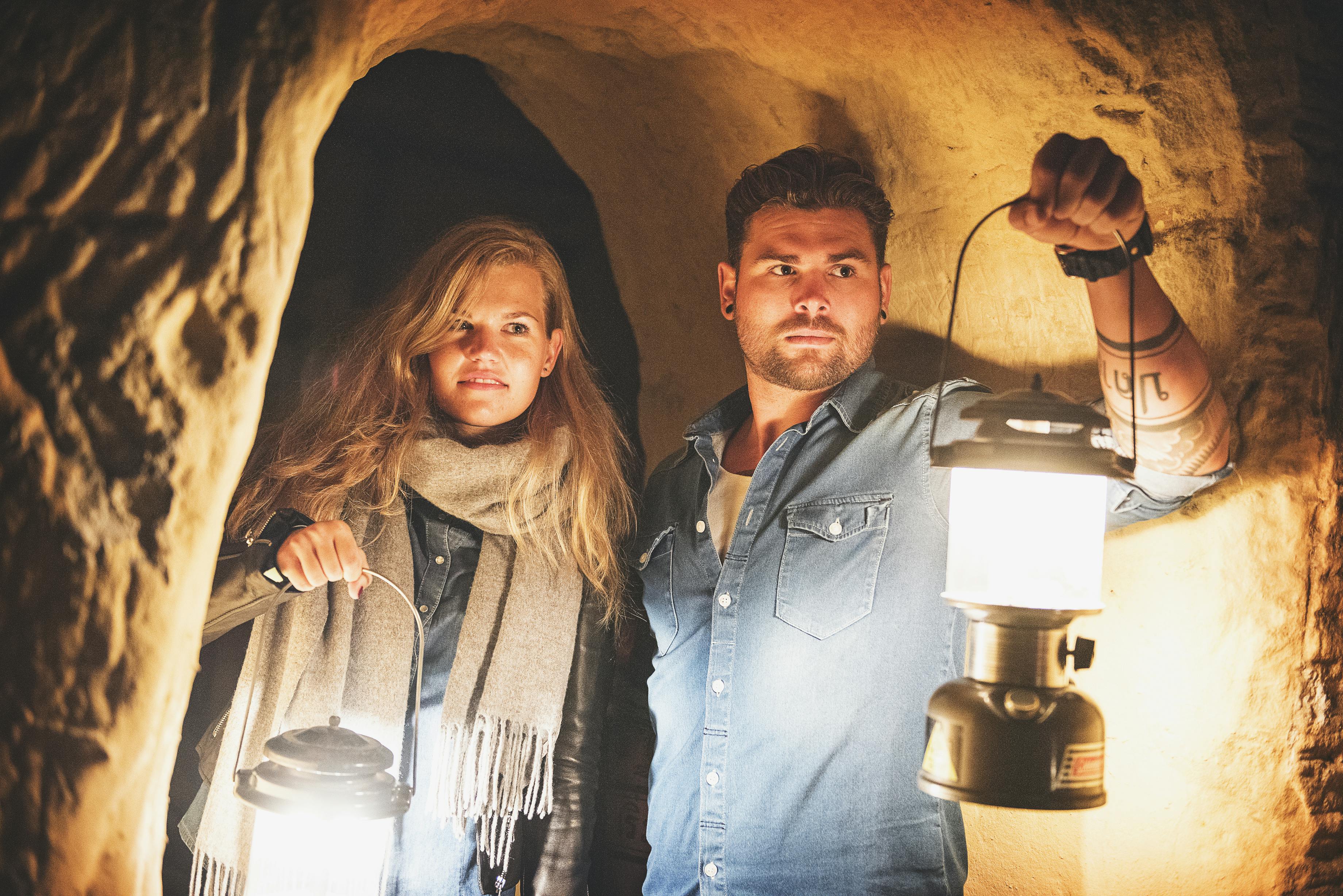 两个拿着灯笼的人站在一个昏暗的洞穴里，凝视着前方。