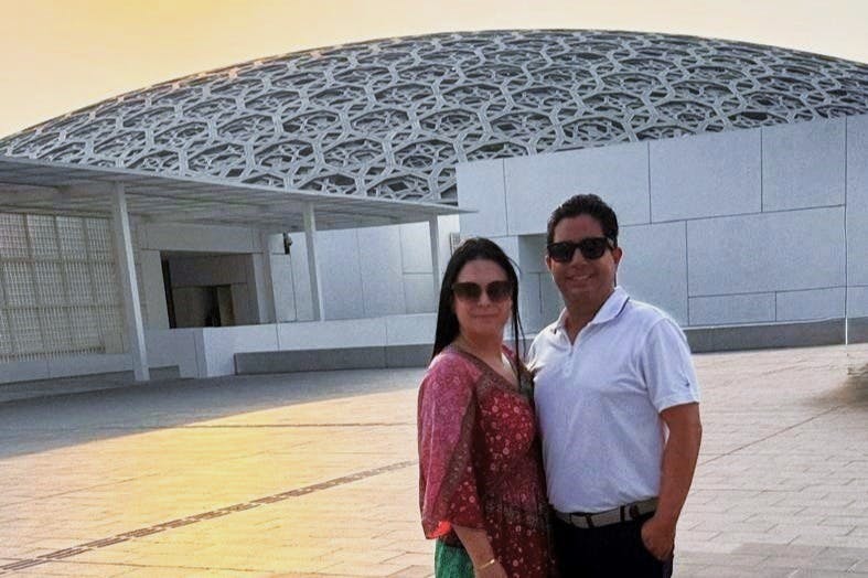 Two people in sunglasses pose for a photo in front of a modern building with a distinctive, intricate dome.