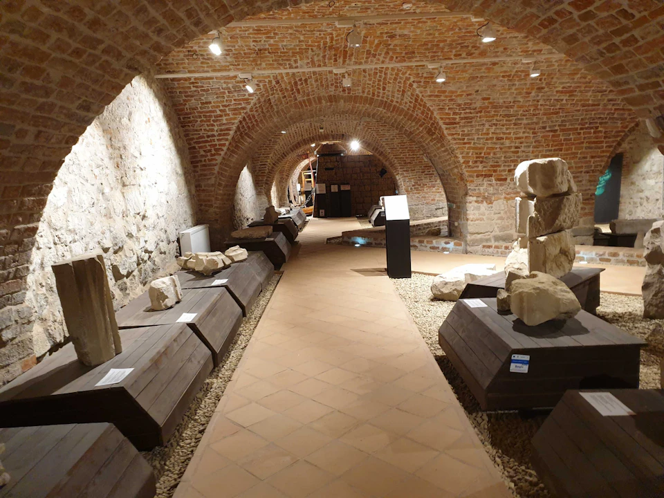 A vaulted brick hallway features display platforms with ancient stone artifacts on both sides, softly illuminated by overhead lights.