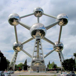 Stor metallisk struktur med sammankopplade sfärer och stödstavar under en molnig himmel, med människor och bilar vid basen.