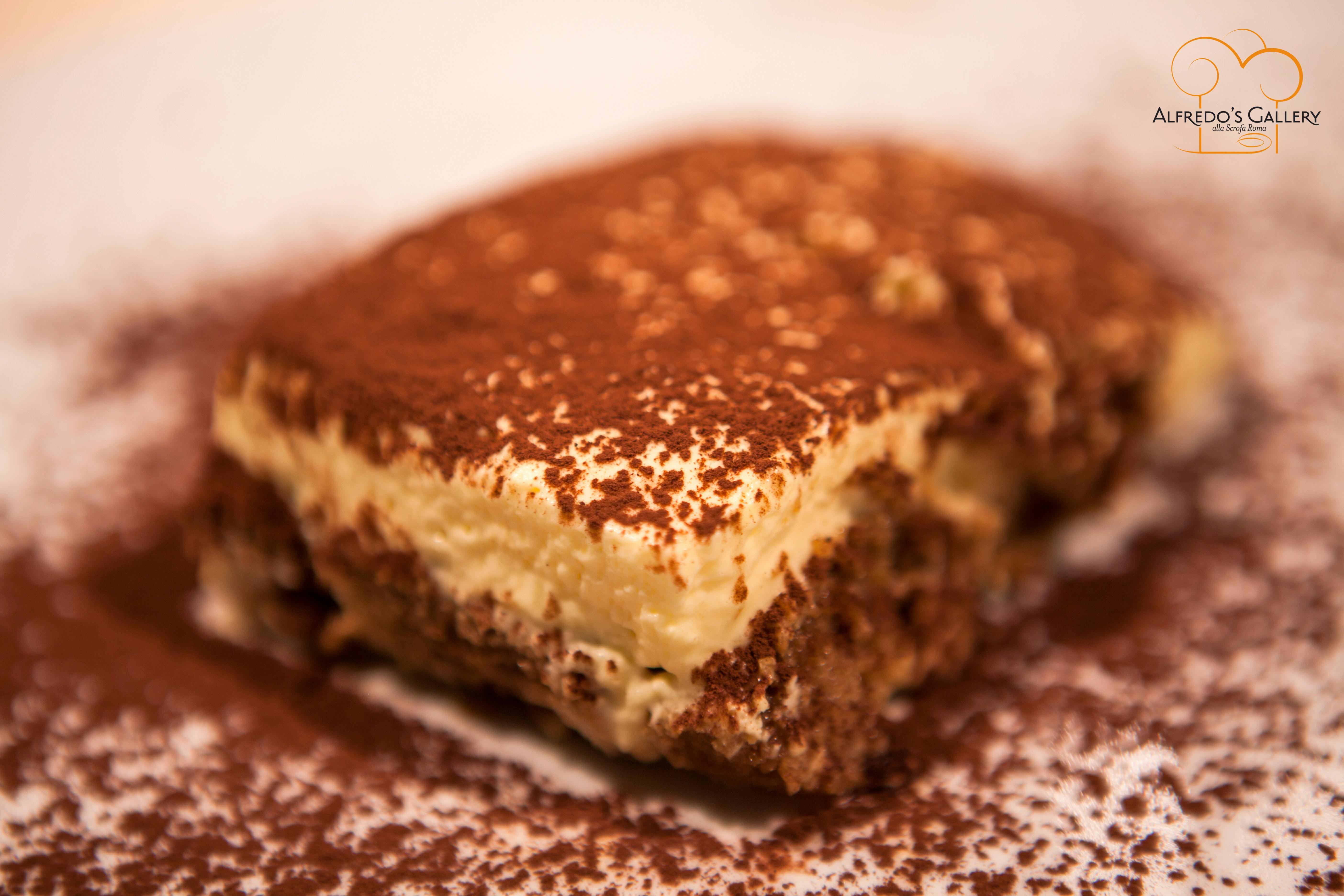 Крупный план кусочка тирамису, посыпанного какао-порошком, на тарелке.