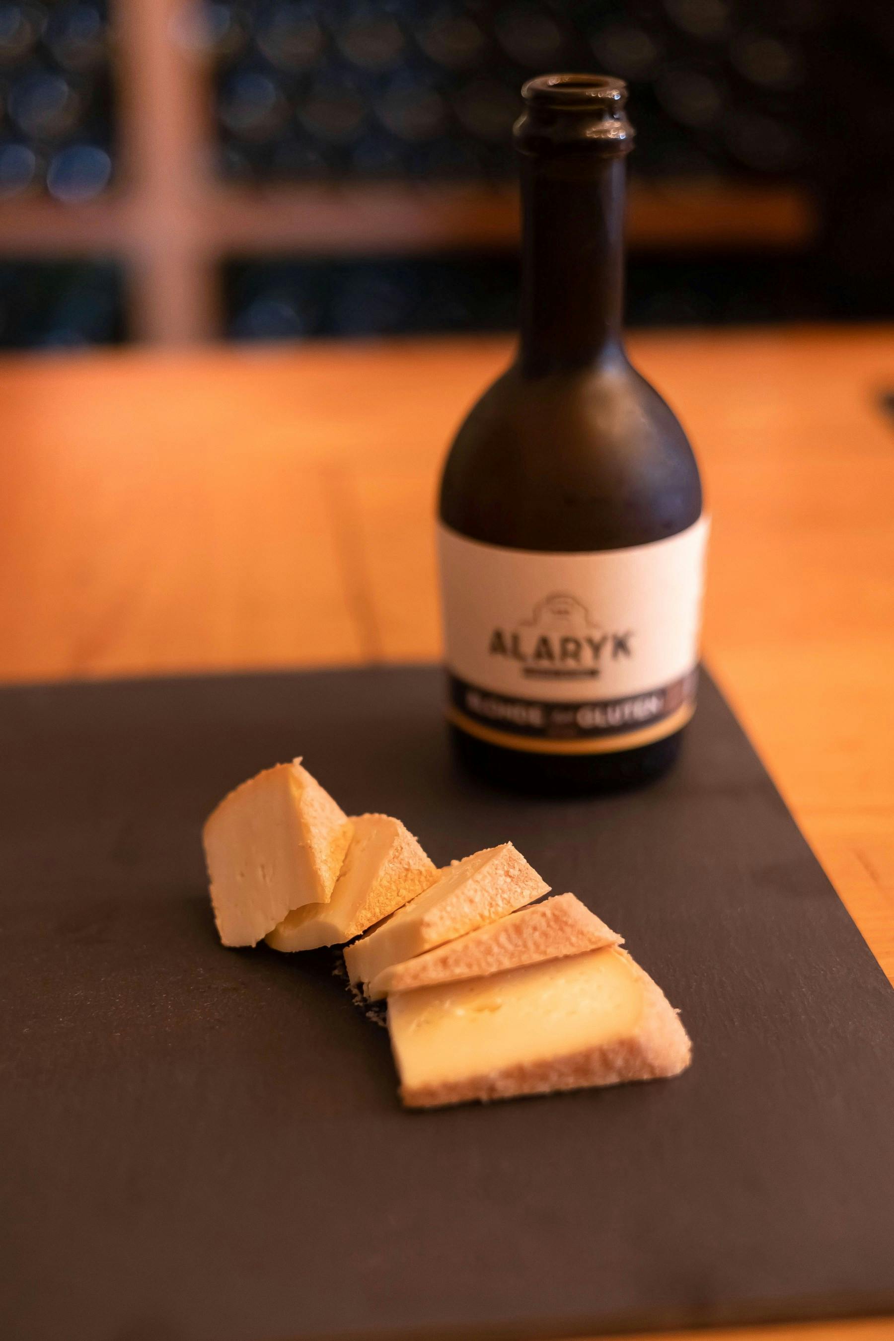 Ломтики сыра на черной поверхности с бутылкой с надписью «Аларык» на заднем плане на деревянном столе.