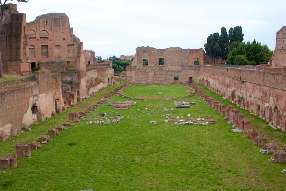 Ancient ruins of a rectangular structure with grassy interior, surrounded by stone walls and remnants of columns.