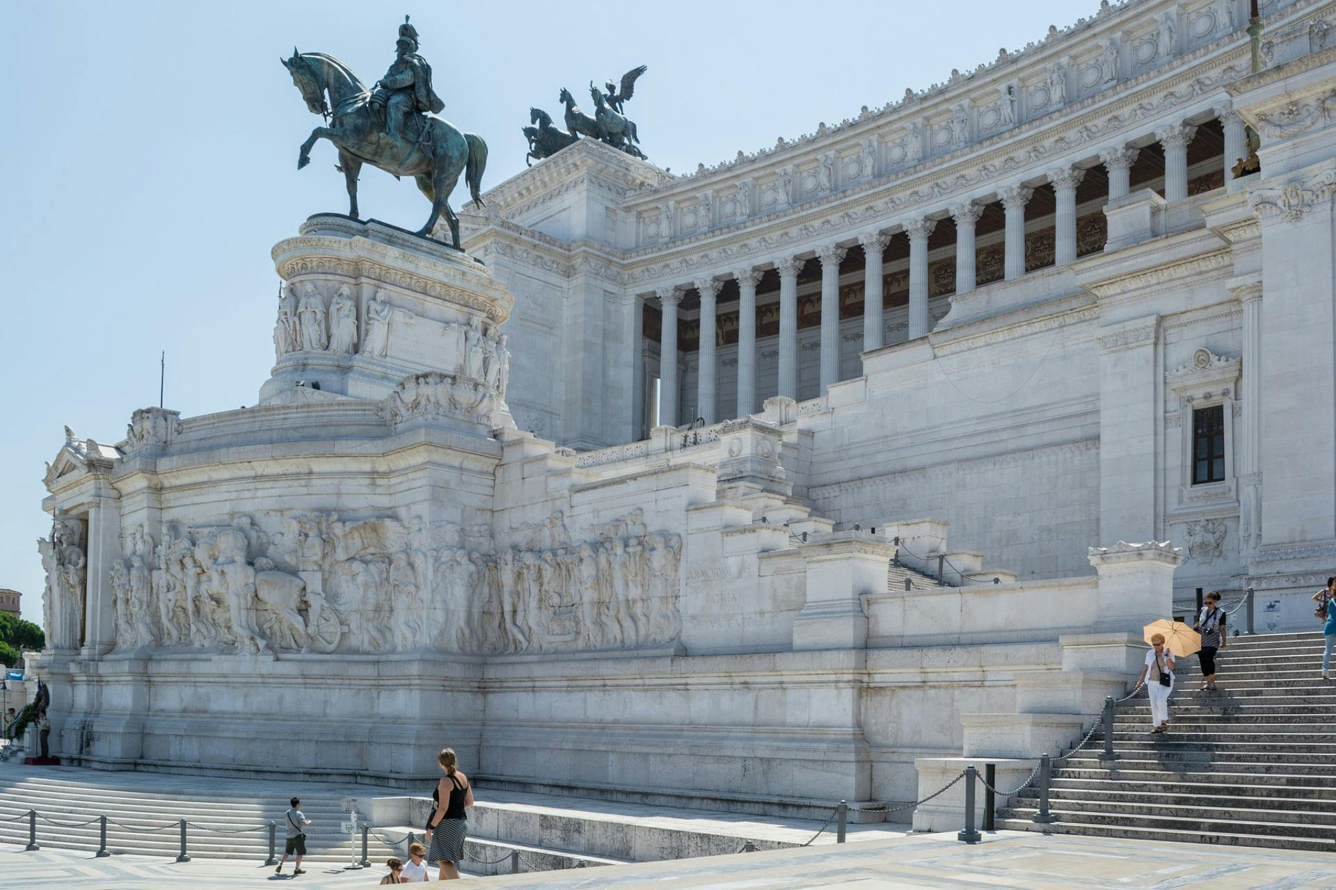 Un grande edificio in marmo con una statua equestre e intricati rilievi. Alcune persone camminano sui gradini in primo piano.