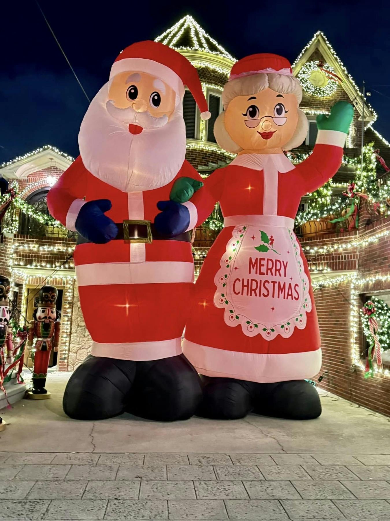 Inflatable Santa Claus and Mrs. Claus decorations in front of a house adorned with Christmas lights at night.