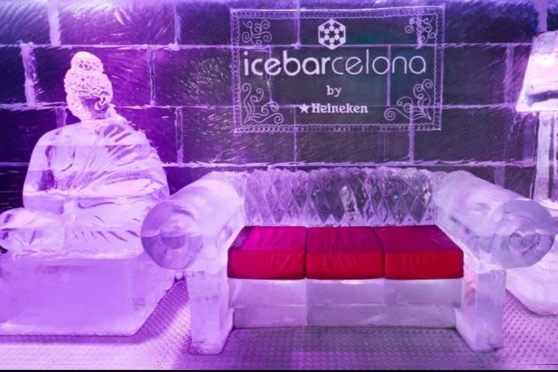 Un canapé en forme de sculpture de glace avec des coussins rouges dans une pièce où l'on peut lire "Ice Barcelona by Heineken".