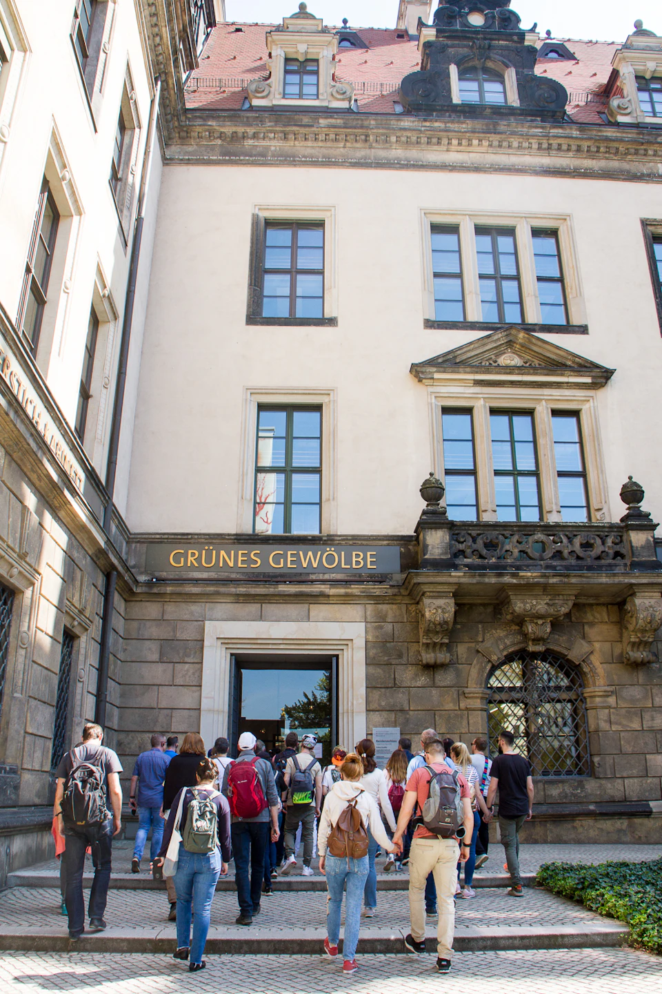 People in front of the entrance to Grünes Gewölbe, a building with large windows and a sign above an arched doorway.