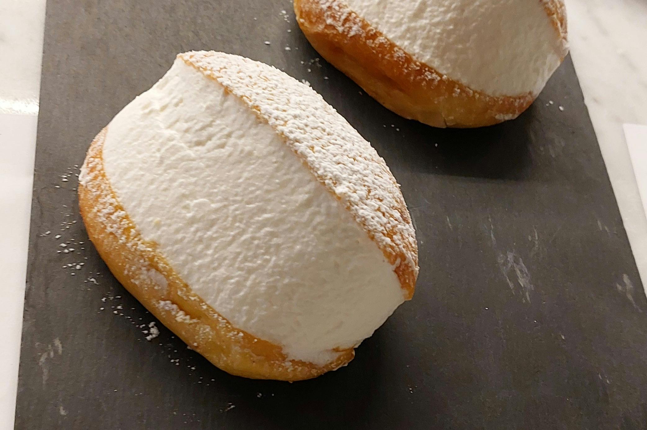 Two cream-filled pastries dusted with powdered sugar on a dark surface.