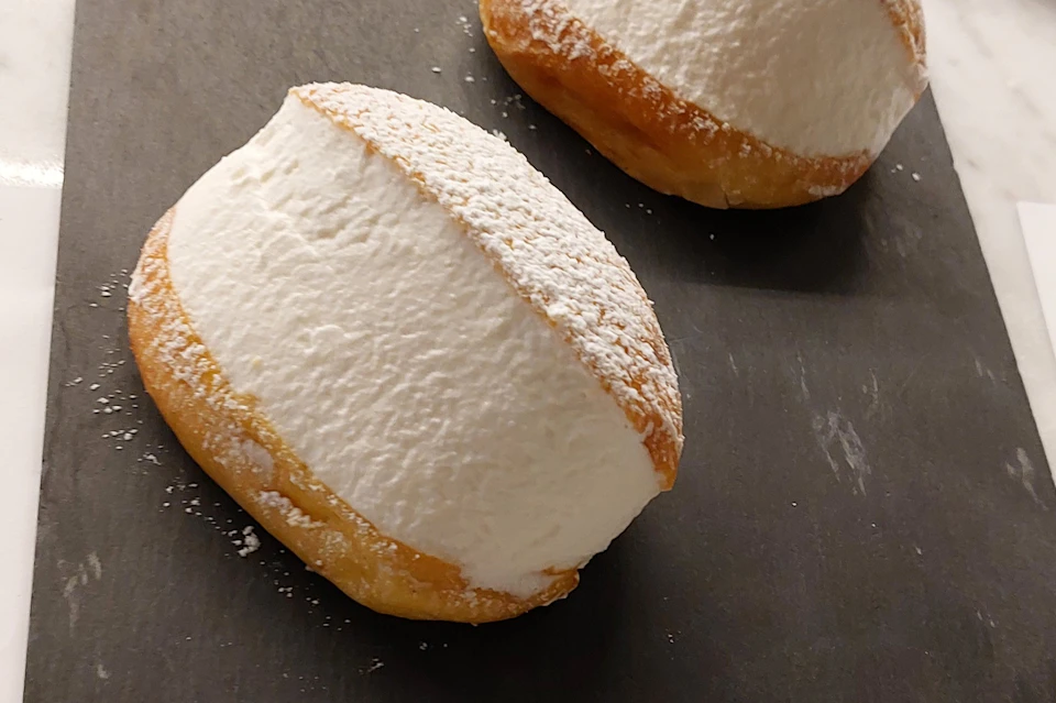 Two cream-filled pastries dusted with powdered sugar on a dark surface.